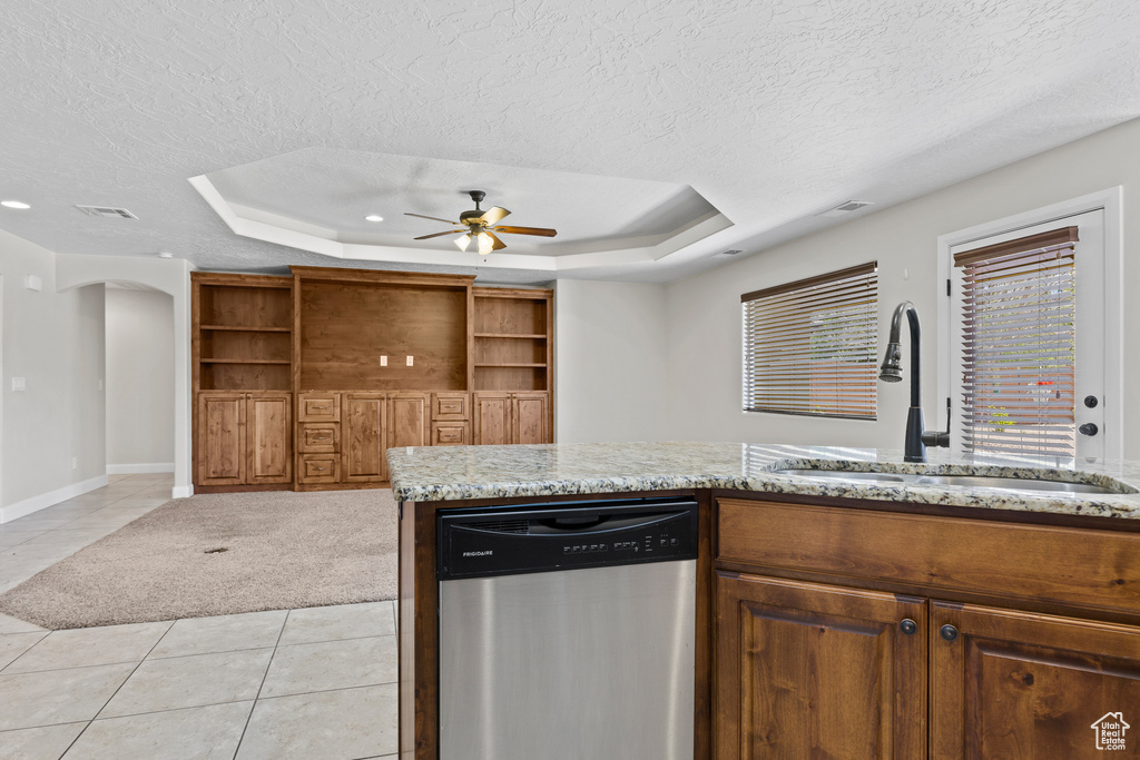 Kitchen with stainless steel dishwasher, a textured ceiling, a sink, a tray ceiling, and light tile patterned floors