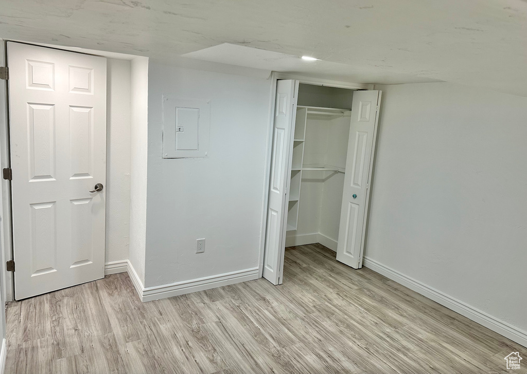 Unfurnished bedroom with electric panel, light wood-style floors, baseboards, and a closet