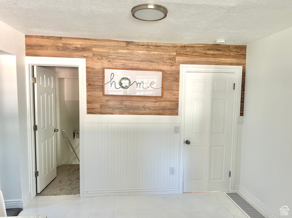Hall featuring wooden walls, a textured ceiling, baseboards, and a wainscoted wall