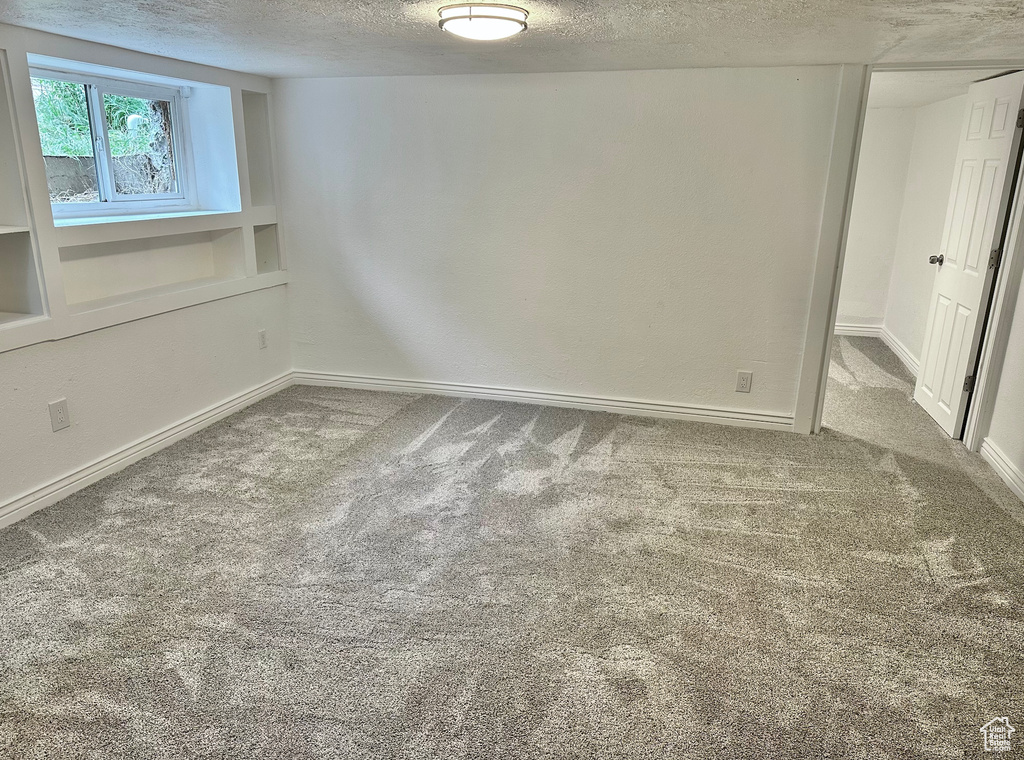 Carpeted empty room featuring a textured ceiling and baseboards
