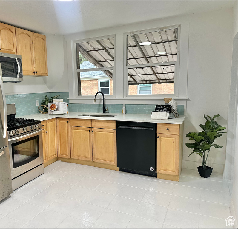 Kitchen with appliances with stainless steel finishes, a sink, light countertops, and decorative backsplash