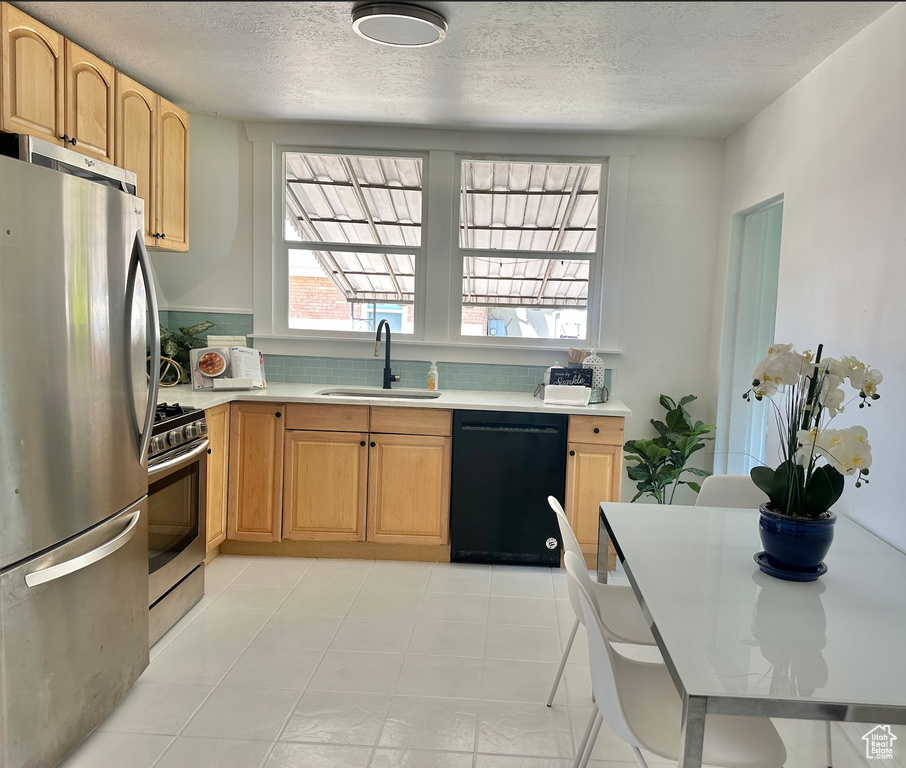 Kitchen with appliances with stainless steel finishes, a sink, a textured ceiling, light countertops, and light brown cabinetry