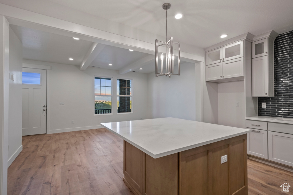Kitchen featuring beamed ceiling, a center island, a chandelier, glass insert cabinets, and light wood-type flooring