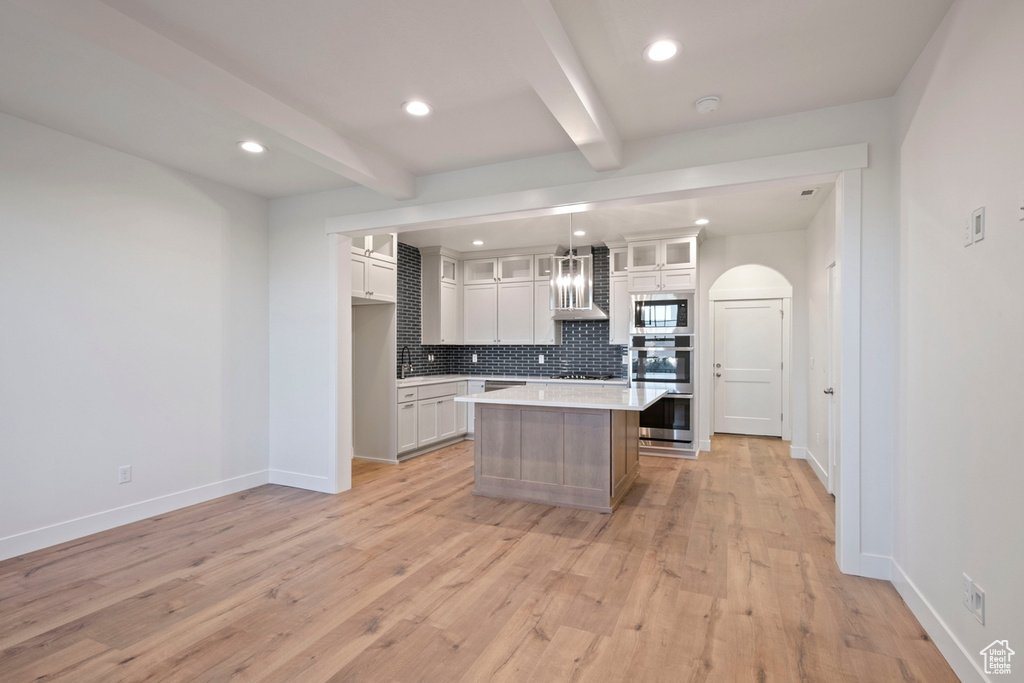 Kitchen with appliances with stainless steel finishes, beamed ceiling, decorative backsplash, light countertops, and white cabinets