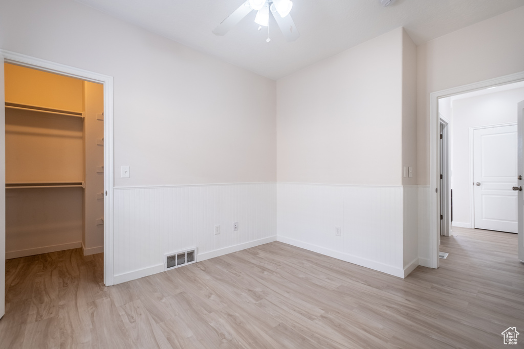 Unfurnished bedroom featuring a spacious closet, wood finished floors, wainscoting, a closet, and a ceiling fan