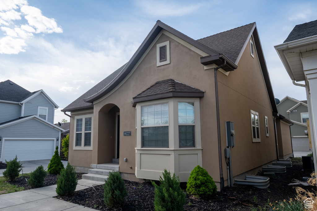 View of front of home with stucco siding, an outbuilding, a garage, and roof with shingles