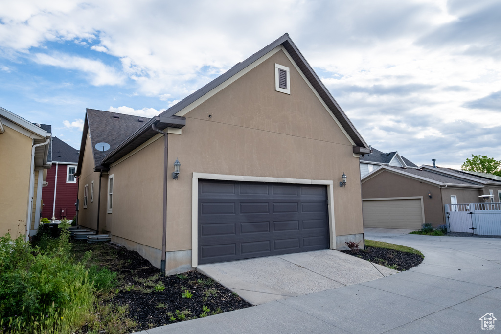 View of side of property featuring driveway, an attached garage, stucco siding, and a gate