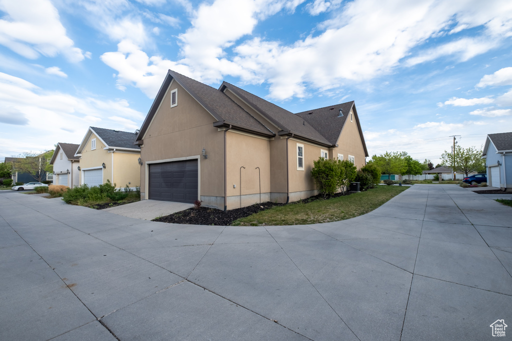 View of side of property with concrete driveway, an attached garage, a residential view, stucco siding, and a shingled roof