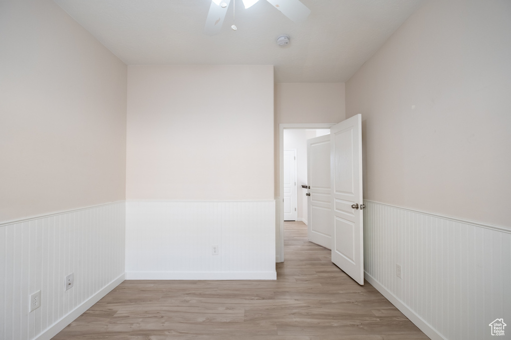 Spare room with wainscoting, light wood finished floors, a ceiling fan, and a smoke detector