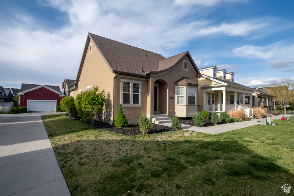 View of front of home with covered porch, stucco siding, a shingled roof, and a front lawn