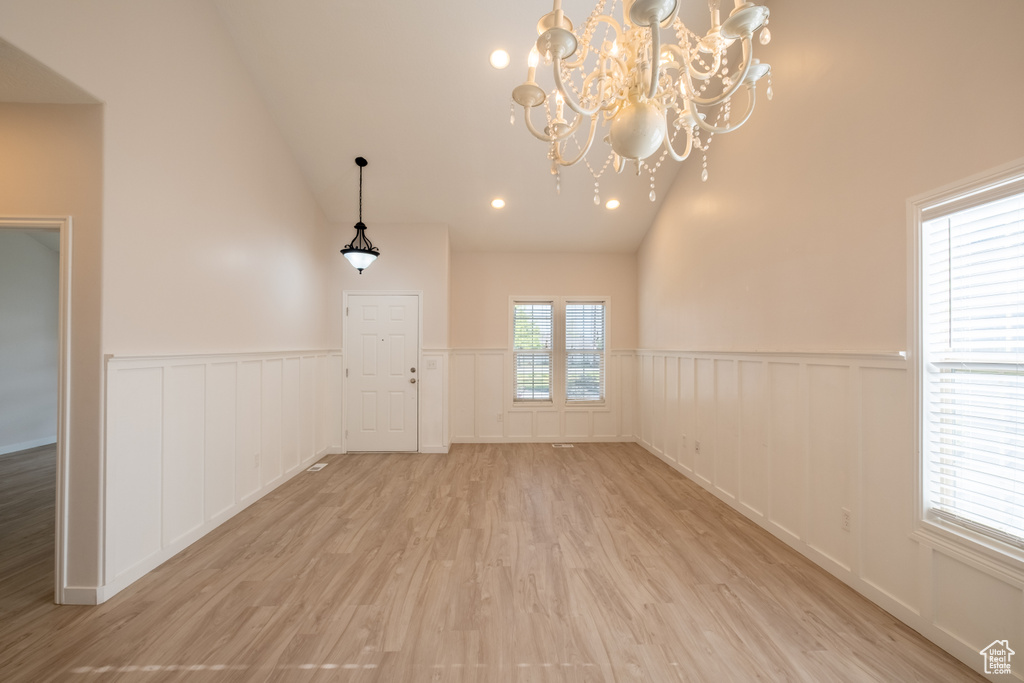 Empty room featuring a chandelier, light wood-style flooring, a wainscoted wall, a decorative wall, and high vaulted ceiling