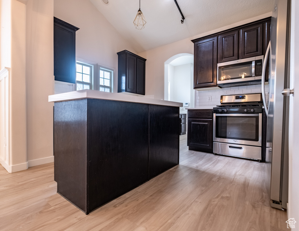Kitchen with stainless steel appliances, light wood-style floors, arched walkways, decorative backsplash, and lofted ceiling