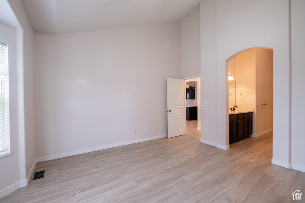 Spare room featuring arched walkways, a sink, light wood-style floors, a towering ceiling, and baseboards