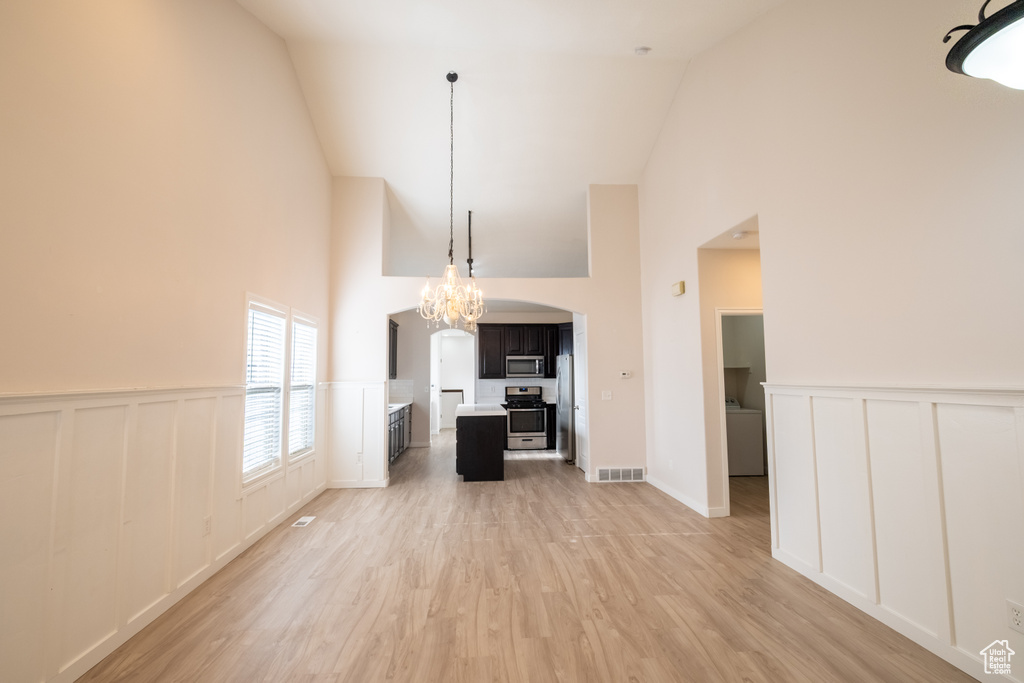 Unfurnished living room featuring high vaulted ceiling, a decorative wall, light wood finished floors, a wainscoted wall, and arched walkways
