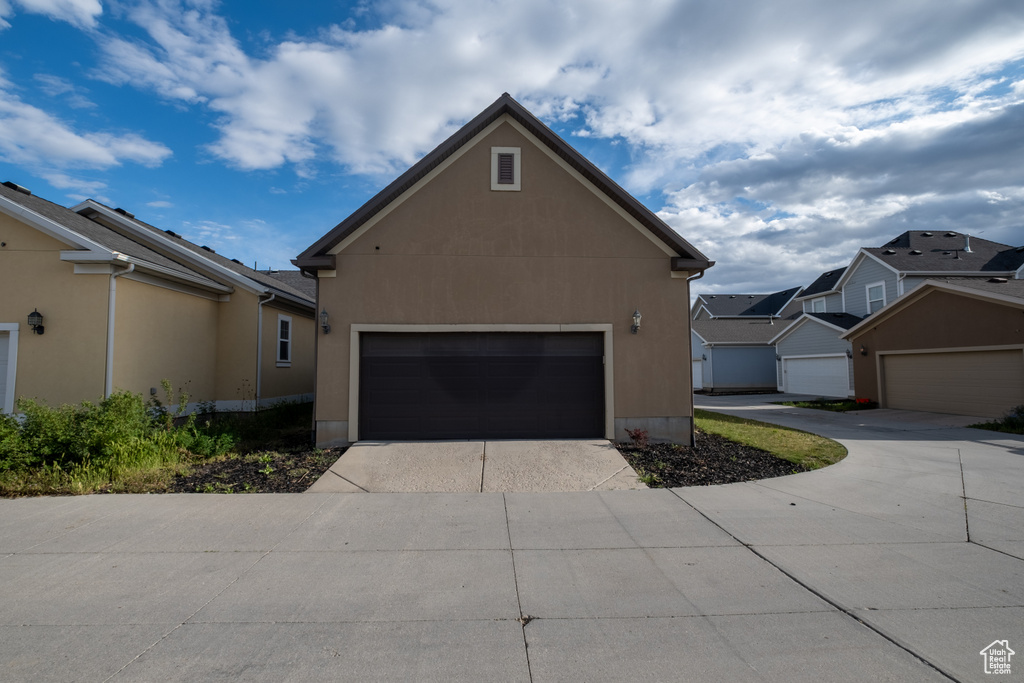View of side of property with driveway, stucco siding, a residential view, and a garage