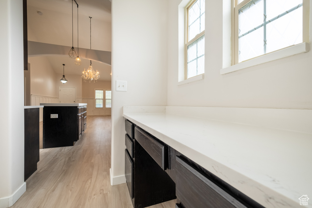 Hallway featuring light wood-style flooring, a chandelier, baseboards, and a towering ceiling