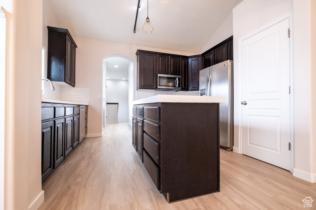 Kitchen featuring appliances with stainless steel finishes, arched walkways, a kitchen island, backsplash, and light wood-type flooring