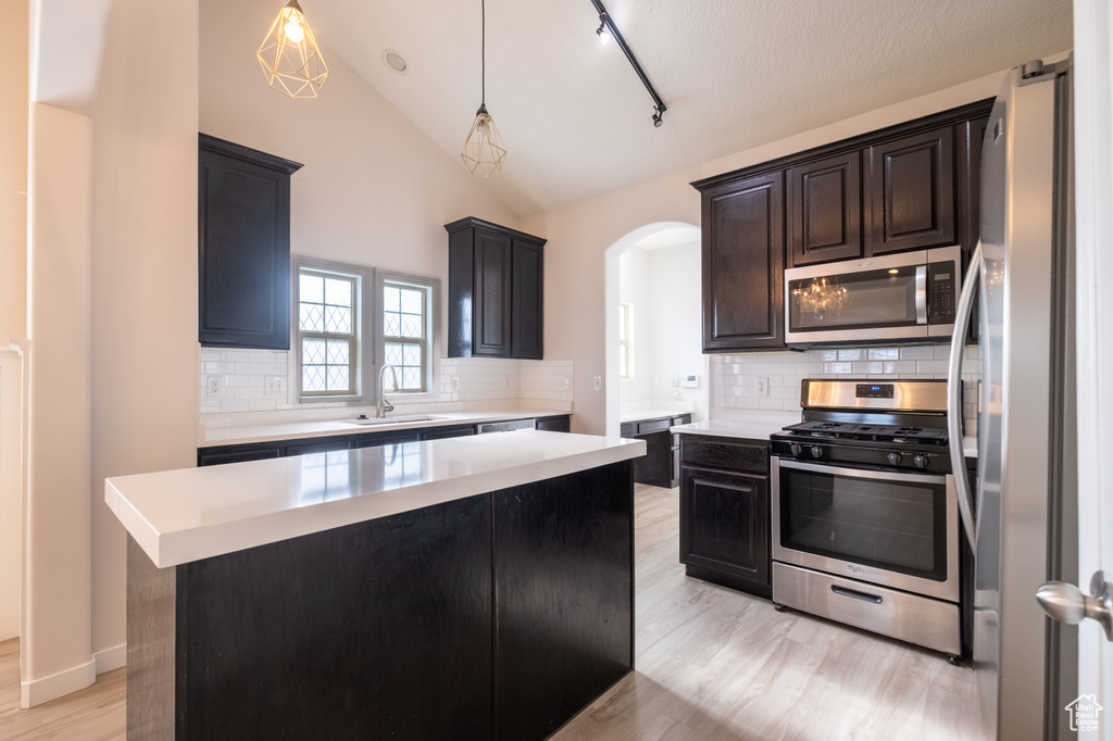 Kitchen featuring stainless steel appliances, a sink, light countertops, arched walkways, and light wood-type flooring