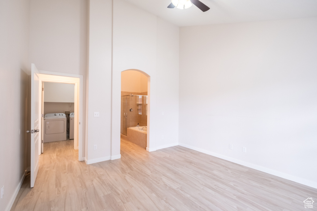 Unfurnished bedroom featuring independent washer and dryer, light wood-style flooring, arched walkways, baseboards, and a towering ceiling
