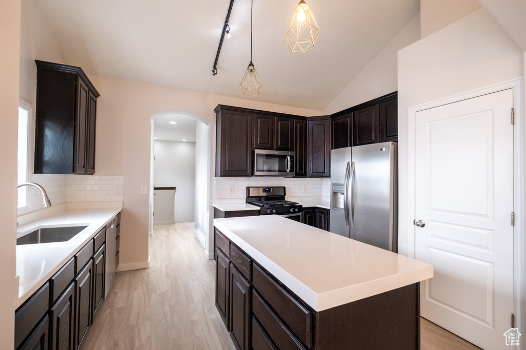 Kitchen featuring stainless steel appliances, a sink, arched walkways, decorative backsplash, and lofted ceiling