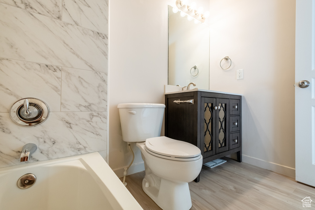 Full bath with a bath, baseboards, wood finished floors, vanity, and toilet