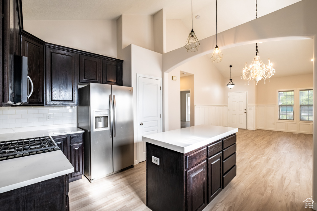 Kitchen with appliances with stainless steel finishes, light wood-style flooring, arched walkways, light countertops, and wainscoting