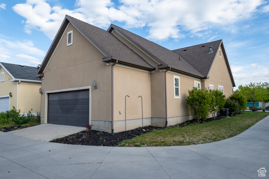 View of side of home with concrete driveway, an attached garage, central air condition unit, roof with shingles, and stucco siding