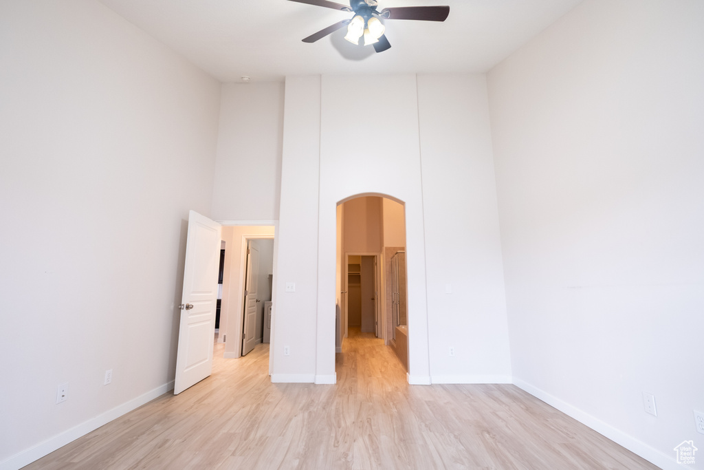 Spare room with arched walkways, a ceiling fan, light wood-style flooring, baseboards, and a towering ceiling