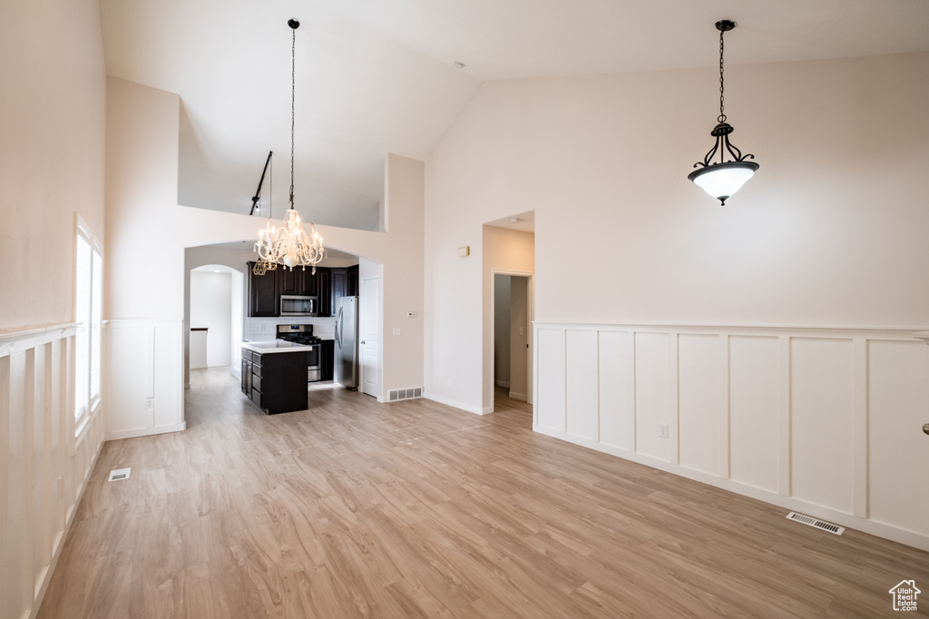 Unfurnished living room with a decorative wall, high vaulted ceiling, a wainscoted wall, light wood-style flooring, and a chandelier