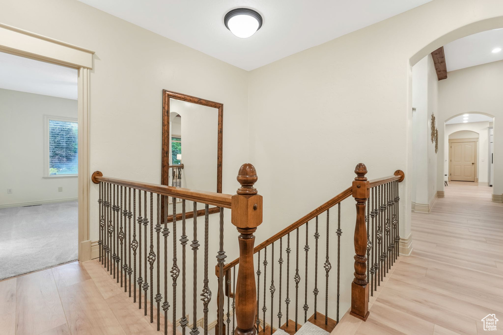 Corridor with wood finished floors, an upstairs landing, arched walkways, and baseboards