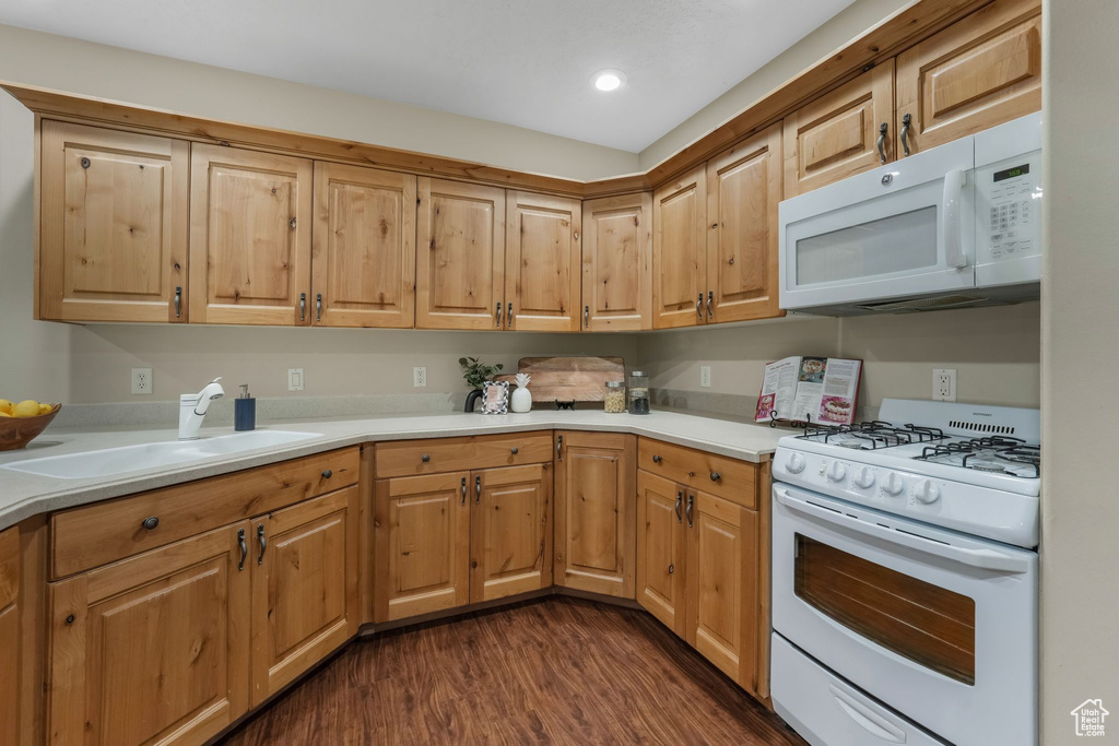 Kitchen with white appliances, a sink, dark wood finished floors, light countertops, and recessed lighting