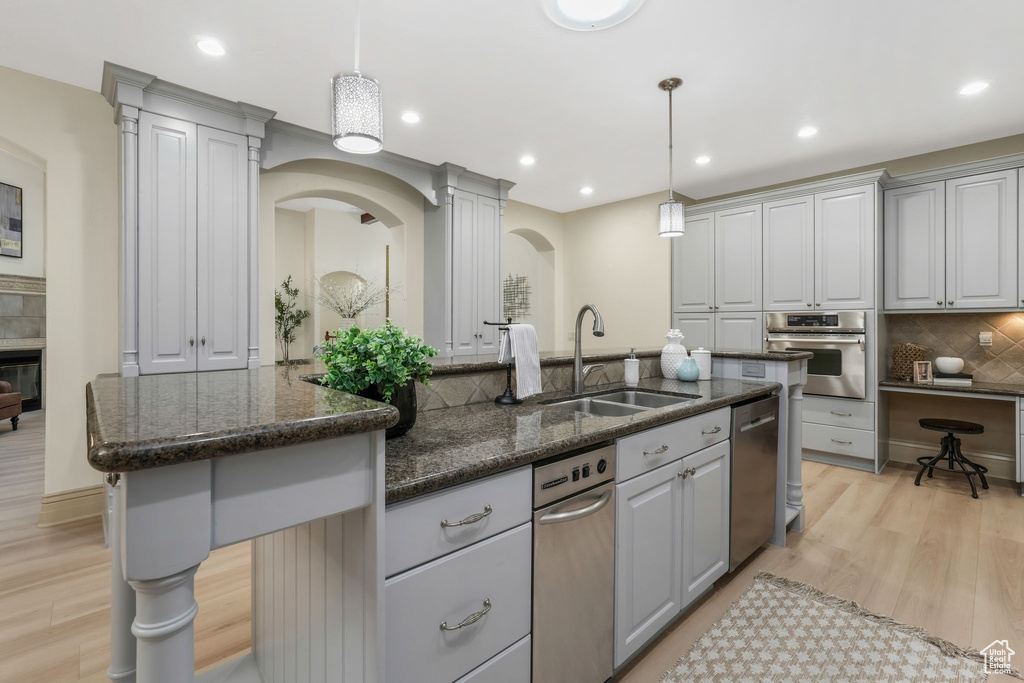 Kitchen with appliances with stainless steel finishes, a sink, gray cabinets, light wood-style floors, and recessed lighting