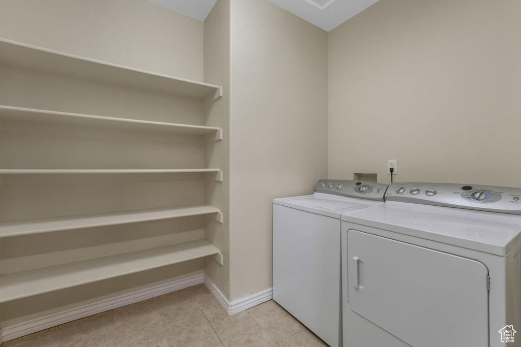 Washroom featuring washing machine and clothes dryer, light tile patterned floors, and baseboards