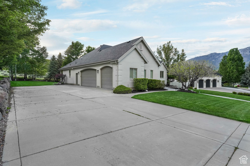 View of property exterior featuring driveway, a lawn, a garage, a mountain view, and roof with shingles