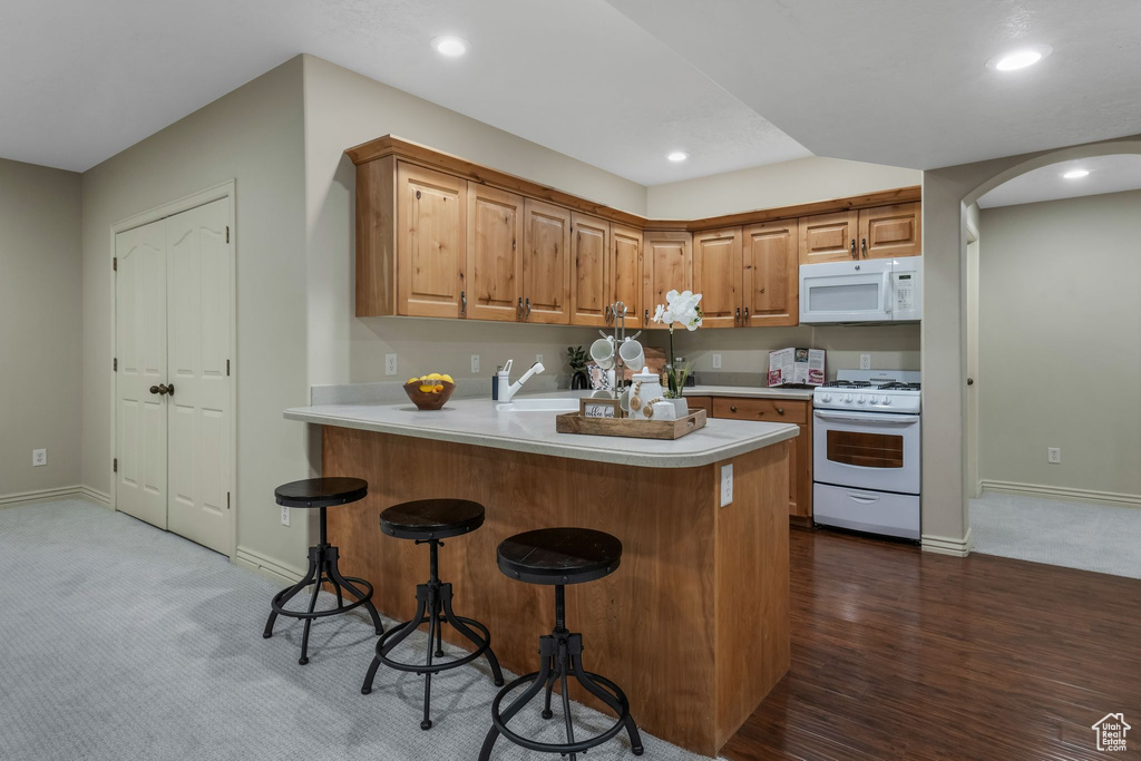 Kitchen featuring white appliances, baseboards, light countertops, a peninsula, and arched walkways