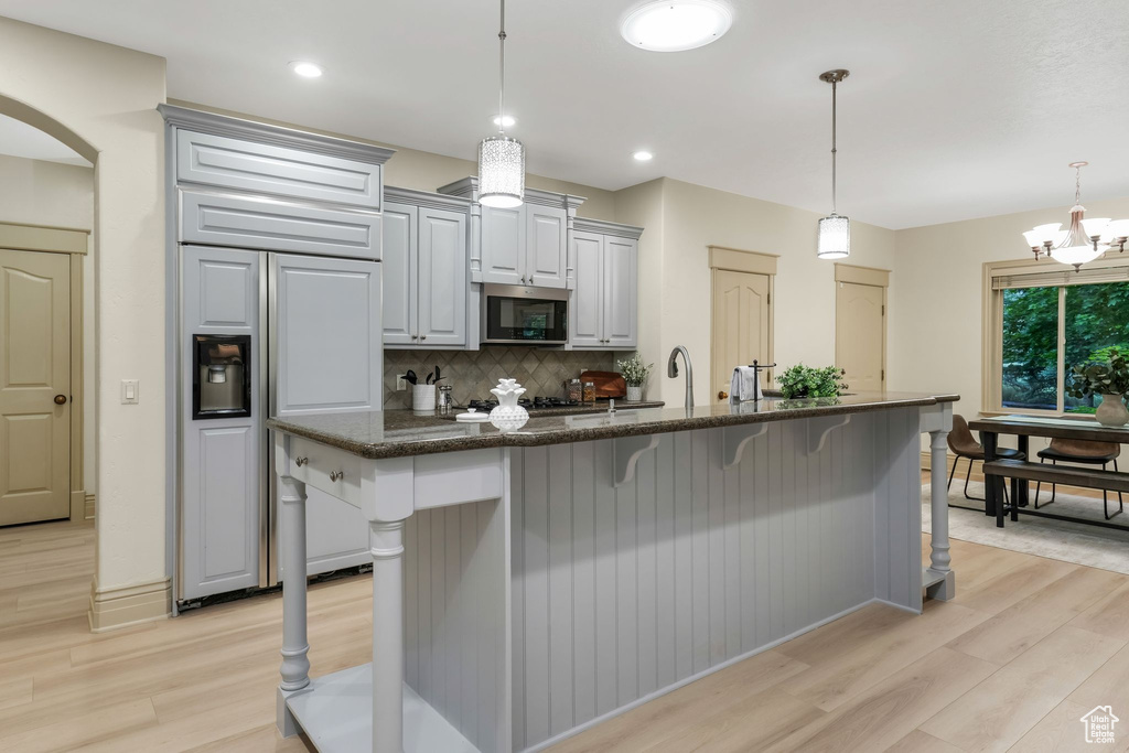 Kitchen featuring stainless steel microwave, paneled built in fridge, light wood-style flooring, a breakfast bar, and recessed lighting