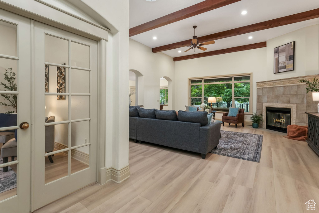 Living area with arched walkways, beamed ceiling, wood finished floors, a tiled fireplace, and a ceiling fan