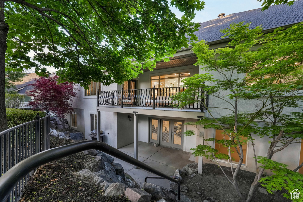 Back of house featuring a balcony, stucco siding, french doors, and a patio