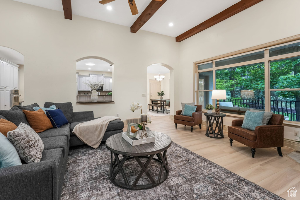 Living area featuring arched walkways, light wood-type flooring, beamed ceiling, ceiling fan, and plenty of natural light