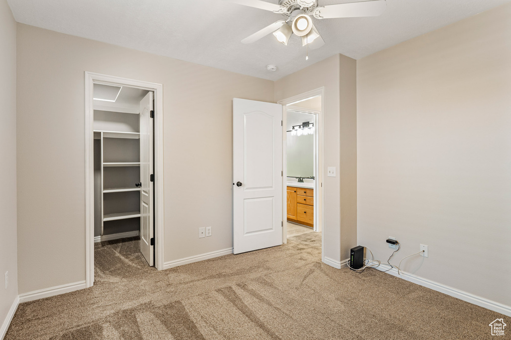 Unfurnished bedroom featuring light carpet, a spacious closet, baseboards, and ceiling fan
