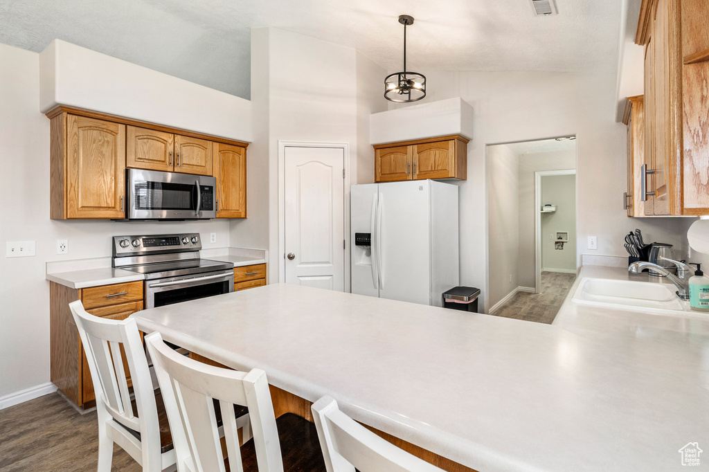 Kitchen with appliances with stainless steel finishes, lofted ceiling, a peninsula, baseboards, and light wood-style flooring