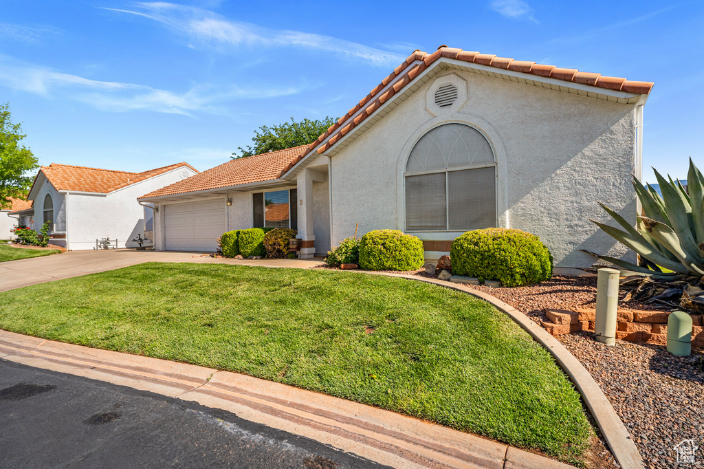 Mediterranean / spanish home with a front yard, a tile roof, driveway, and stucco siding