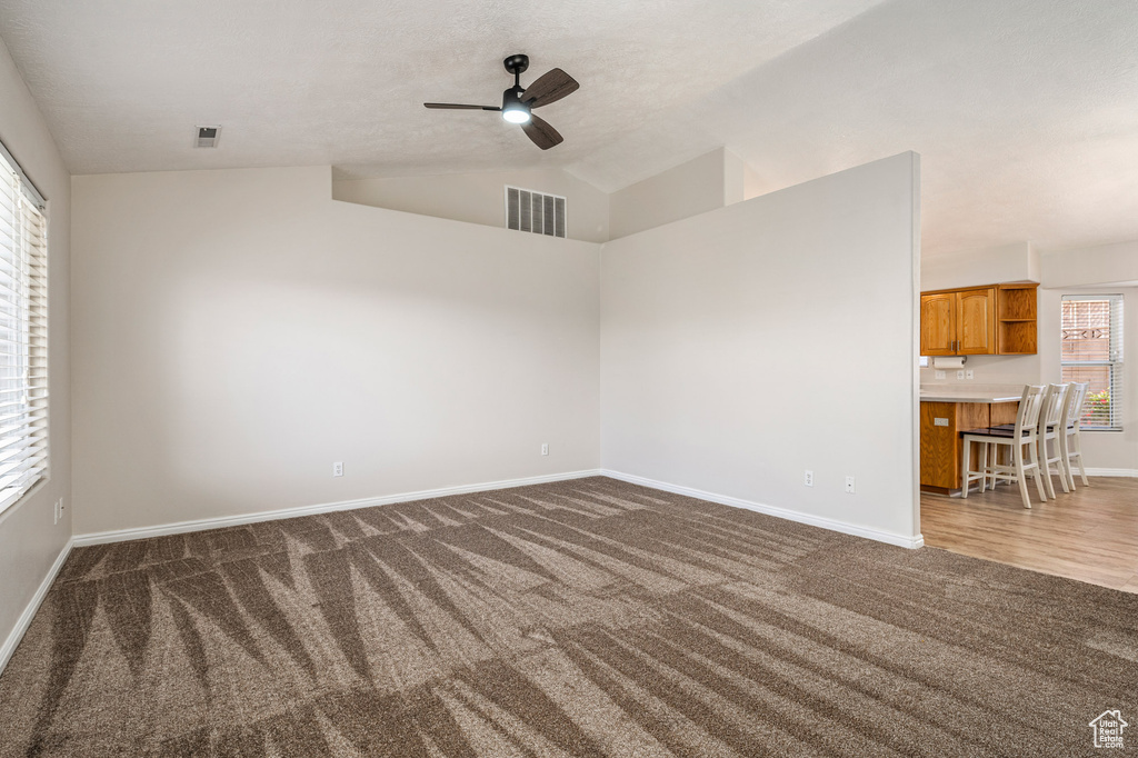 Empty room with dark colored carpet, a ceiling fan, baseboards, and lofted ceiling