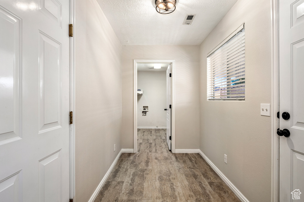Hall with wood finished floors, baseboards, and a textured ceiling