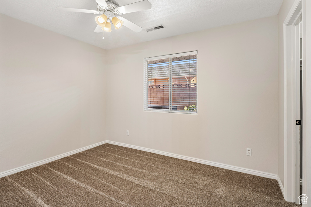 Empty room with dark colored carpet, baseboards, and a ceiling fan