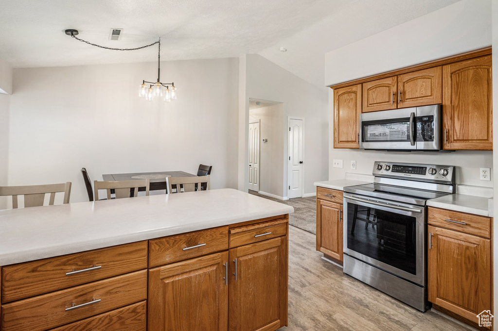 Kitchen featuring stainless steel appliances, lofted ceiling, a chandelier, light countertops, and brown cabinetry