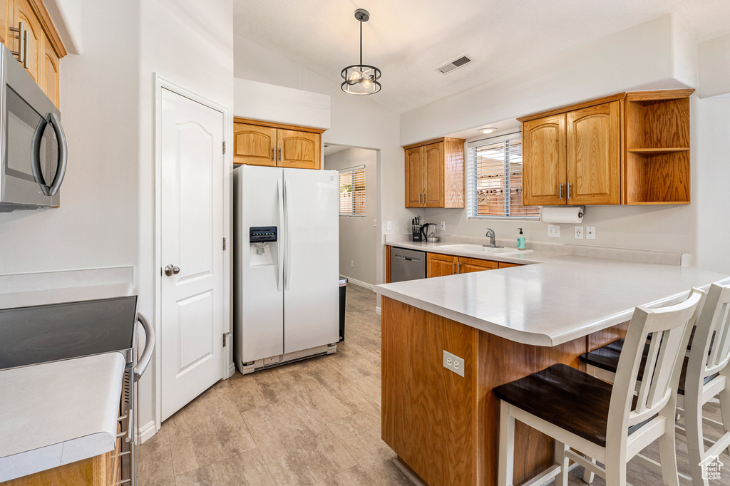 Kitchen featuring appliances with stainless steel finishes, a kitchen breakfast bar, a sink, a peninsula, and lofted ceiling