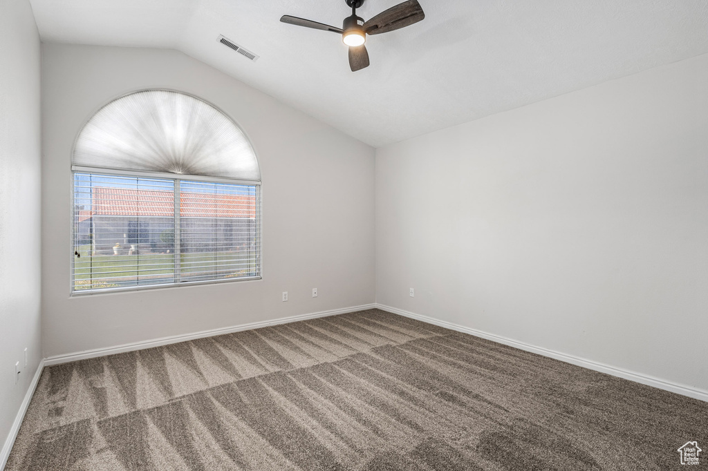 Carpeted empty room featuring a ceiling fan, vaulted ceiling, and baseboards