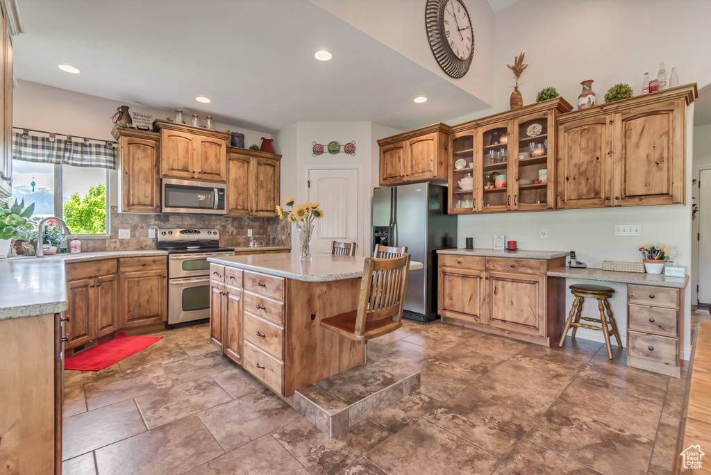 Kitchen featuring appliances with stainless steel finishes, a sink, tasteful backsplash, glass insert cabinets, and recessed lighting