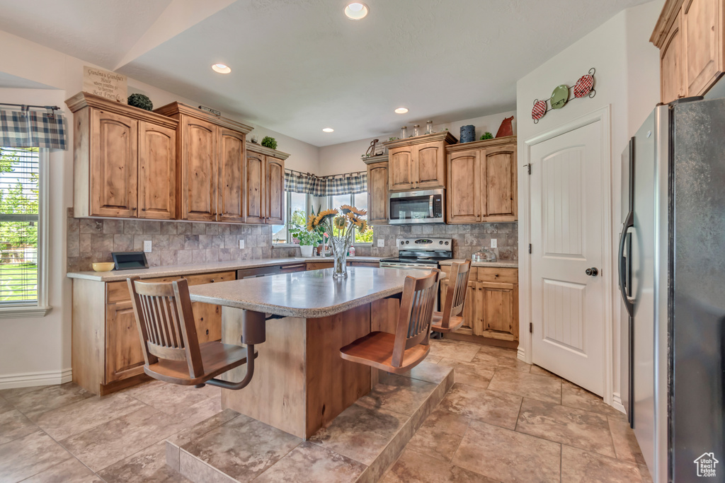 Kitchen featuring appliances with stainless steel finishes, backsplash, a kitchen island, light countertops, and a kitchen breakfast bar